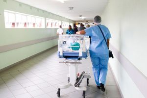 male nurse in scrubs walking down a hospital hallway with equipment