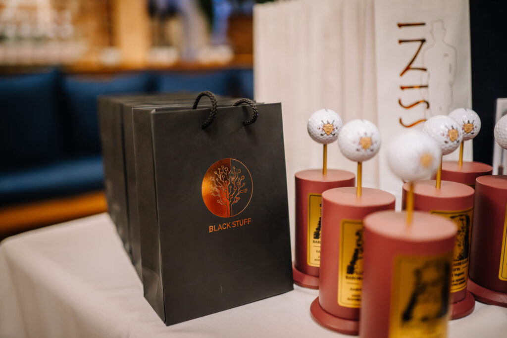 Black, red, and gold branded bags and other event giveaways are arranged on a table.